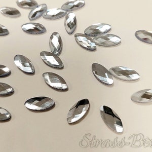 May include: A scattering of silver oval-shaped rhinestones on a light beige surface.