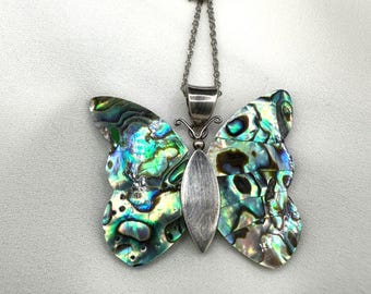 May include: A butterfly pendant necklace with iridescent wings in shades of green, blue, and silver. The butterfly's body is a silver-toned metal. The necklace chain is also silver-toned.