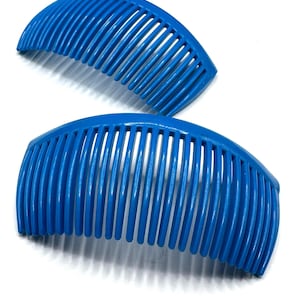 May include: Two bright blue hair combs are displayed against a white background. The combs have a curved design with evenly spaced teeth. The plastic combs are a vibrant shade of blue, and the image is well-lit, highlighting the details of the combs.