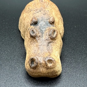 Puede incluir: Figura de hipopótamo de cerámica en tonos marrones. La escultura tiene una superficie texturizada y detalles, incluyendo fosas nasales prominentes y orejas pequeñas. Es un objeto decorativo.