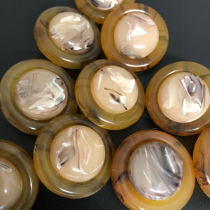 Op de afbeelding: Een set van acht ronde, bruin-witte knoppen met een marmerpatroon. De knoppen hebben een verhoogde, getextureerde rand.