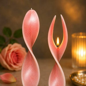 Könnte beinhalten: Zwei hohe, rosafarbene, gedrehte Kerzen mit einer glatten, matten Oberfläche. Eine Kerze ist nicht angezündet und hat eine durchgehende Spiralform. Die zweite Kerze brennt mit einer Flamme zwischen zwei nach oben gebogenen Spitzen.