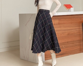 May include: A woman wearing a beige turtleneck sweater and a black and white plaid skirt. She is wearing white ankle boots and is standing in front of a wooden counter.