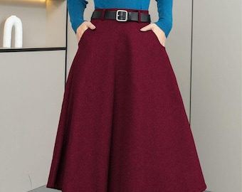 May include: A teal long-sleeve sweater paired with a burgundy midi skirt, cinched at the waist with a black belt. The skirt has pockets and a flared silhouette. The outfit is completed with black tights and shoes.