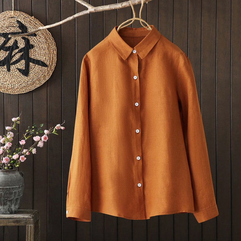 May include: A long-sleeved, button-down shirt in a burnt orange color. The shirt is made of a linen fabric and has a classic, relaxed fit.