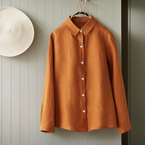 May include: A long-sleeved, rust-colored linen shirt with a button-up front and a classic collar.