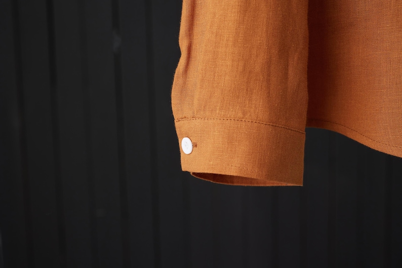 May include: A long-sleeved shirt with a button cuff in a rust orange color. The shirt is made of a linen fabric.