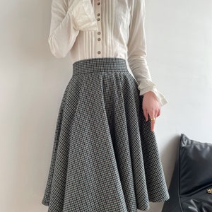May include: A white long-sleeved blouse with a high collar and button detailing, paired with a black and white checkered skirt.