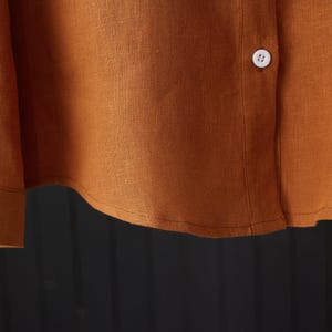 May include: Close-up of the bottom hem of a rust-colored linen shirt with a white button.