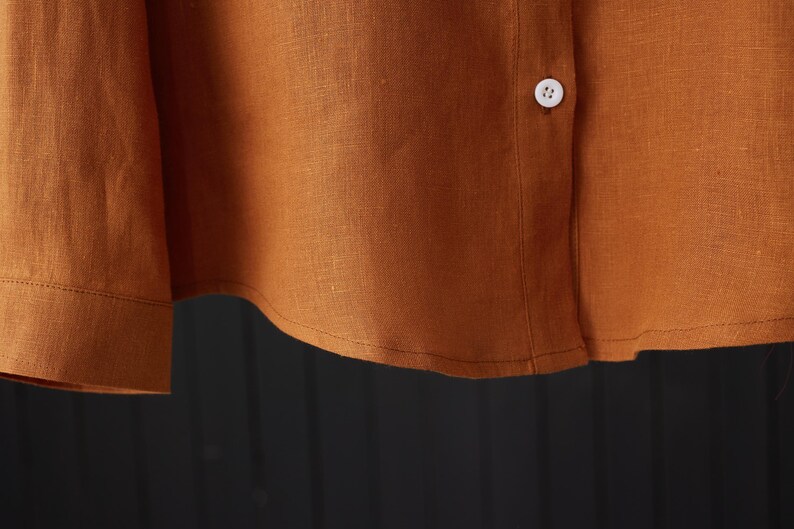 May include: Close-up of the bottom hem of a rust-colored linen shirt with a white button.