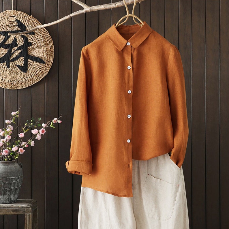May include: A long-sleeved, button-down shirt in a burnt orange color. The shirt is made of a linen fabric and has a relaxed fit.