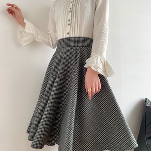 May include: A white long-sleeved blouse with a ruffled collar and cuffs, paired with a black and white checkered skirt.