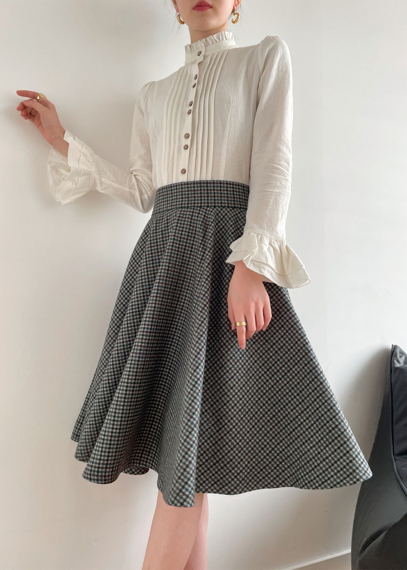 May include: A white long-sleeved blouse with a ruffled collar and cuffs, paired with a black and white checkered skirt.