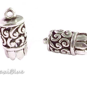 Può includere: Due tappi terminali decorativi in metallo argentato con un intricato design a spirale. I tappi sono lunghi circa 2,5 cm e hanno un anello nella parte superiore.