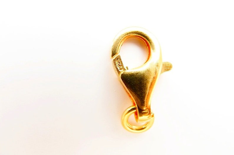 K&ouml;nnte beinhalten: Ein goldfarbener Karabinerverschluss mit einem Federring. Der Verschluss ist mit "925" gekennzeichnet, was bedeutet, dass er aus Sterlingsilber besteht.