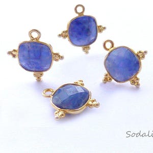 Può includere: Quattro ciondoli in sodalite quadrati color oro. Ogni ciondolo presenta una vibrante pietra preziosa blu incastonata in una montatura dorata con dettagli decorativi. I ciondoli hanno piccoli anelli per il fissaggio.
