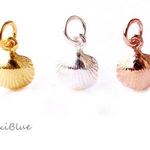 Pode incluir: Três pingentes de concha em ouro, prata e ouro rosa. Cada pingente tem um pequeno laço na parte superior para prender a um colar ou pulseira. Os pingentes são detalhados com texturas caneladas.