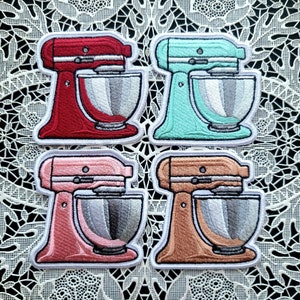 May include: Four embroidered iron-on patches of stand mixers in red, teal, pink, and beige. Each patch features a detailed design of a stand mixer with a bowl.