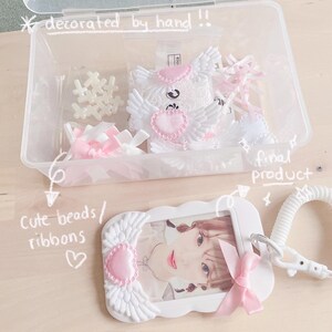 May include: A white plastic frame with pink and white wings and a pink heart. The frame has a photo of a person inside. The frame is attached to a white plastic lanyard with a white plastic clip. The frame is decorated with pink and white ribbons. The text "final product" is written on the image.