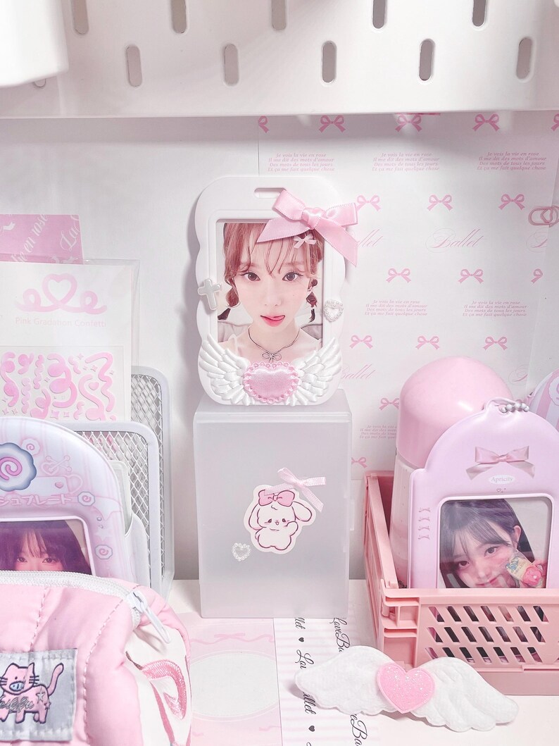 May include: A pink and white plastic storage box with a clear front panel. The box has a small sticker of a cartoon bunny with a pink bow on it. The box is filled with various items, including a small pink and white picture frame with a photo of a young woman, a pink and white water bottle, and a pink and white plastic basket.