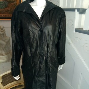 May include: A black leather jacket with a long, fitted silhouette. The jacket has a single button closure and a collar. The sleeves have a contrasting black trim.