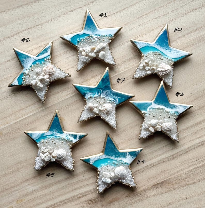 May include: Six gold-rimmed blue and white resin star ornaments with white seashells and glitter. The stars are numbered 1 through 6.
