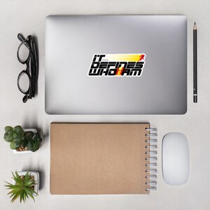May include: A sticker featuring the phrase "IT DEFINES WHO I AM" in a striking black and white font. The design incorporates a running figure with yellow and red streaks, conveying speed. The sticker is placed on a laptop.