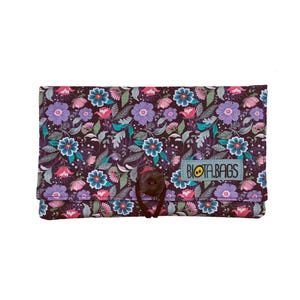 Op de afbeelding: Een bloemenpatroon portemonnee met een donkere achtergrond, met paarse, teal en roze bloemen. De portemonnee heeft een knoopsluiting en een label met de tekst "BIOTA.BAGS". Het ontwerp is een herhalend patroon van bloemen en bladeren.
