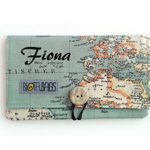 May include: A green fabric pouch with a world map print and a button closure. The pouch has the name "Fiona" printed on the front and the text "Biota.Bags" printed on the bottom.