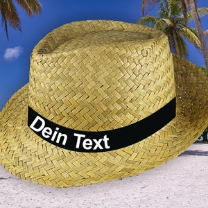 Könnte beinhalten: Ein Strohhut mit einem schwarzen Band und dem Text "Dein Text" in weißen Buchstaben. Der Hut liegt auf einem weißen Sandstrand mit Palmen im Hintergrund.
