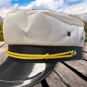 May include: A white captain's hat with a black band and a gold rope trim. The hat has a black visor and a gold button on the side.