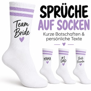 May include: White crew socks with two light purple stripes at the top. The socks feature black text and a small purple heart. The text reads Team Bride, MAMA, #1 DAD, and Beste Freundin. The image also includes the text SPRÜCHE AUF SOCKEN.