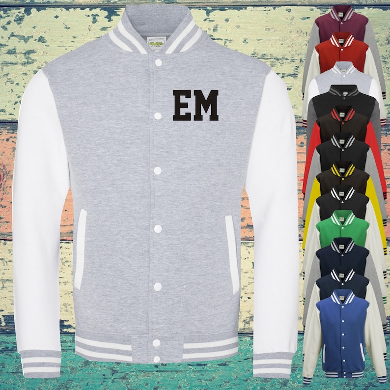 May include: A heather grey varsity jacket with white sleeves and white striped ribbed trim at the collar, cuffs, and hem. The jacket features a front snap button closure and the black letters EM printed on the left chest. A column of various coloured jackets is visible.