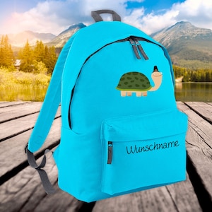 Può includere: Uno zaino blu brillante con una tartaruga verde che indossa un cappello e il testo "Wunschname" sulla tasca anteriore.