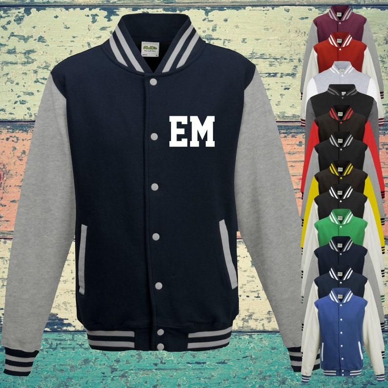 May include: A navy blue varsity jacket with heather grey sleeves, featuring the white letters EM on the left chest. The jacket has a snap-button front, striped ribbed collar, cuffs, and hem, and is displayed alongside a column of various colour options.