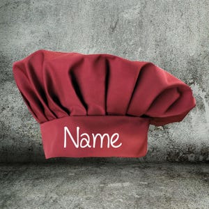 Könnte beinhalten: Eine rote Kochmütze mit dem Wort "Name" in weiß auf der Vorderseite gestickt.
