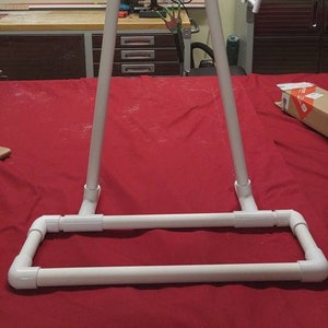 Peut inclure: Un support en PVC blanc avec un cadre triangulaire et une base rectangulaire. Le support est sur une surface rouge.