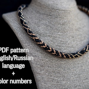 May include: A beaded rope necklace featuring a repeating geometric chevron pattern in black and metallic gold beads. The image includes text stating PDF pattern English/Russian language + Color numbers and the brand name Kaira Bijou.