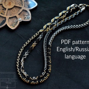 Op de afbeelding: Twee kralenkettingen, een zwart en goud, de andere zilver en zwart, met een PDF-patroon in het Engels en Russisch.
