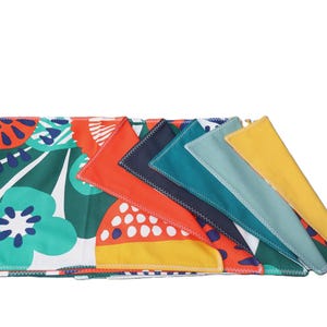 Può includere: Un set di sette tovaglioli di stoffa colorati con una varietà di motivi, tra cui disegni floreali, geometrici e astratti. I tovaglioli sono piegati a forma triangolare e disposti in fila.
