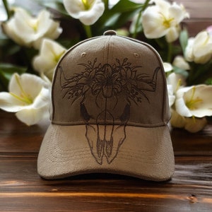 Peut inclure: Une casquette de baseball en daim marron avec un motif floral et un graphique de crâne de taureau.
