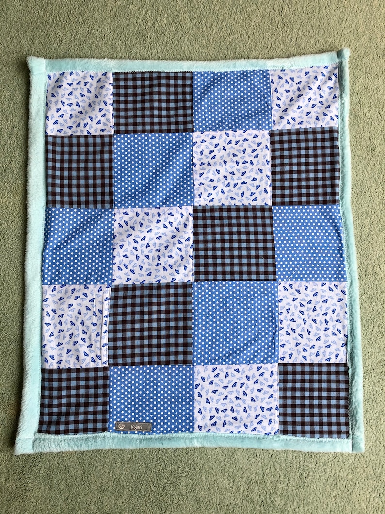 Puede incluir: Una manta de beb&eacute; de patchwork azul y negro con ribete blanco. La manta est&aacute; hecha de diferentes telas con varios patrones, incluyendo lunares, cuadros y un peque&ntilde;o estampado de sombreros azules.