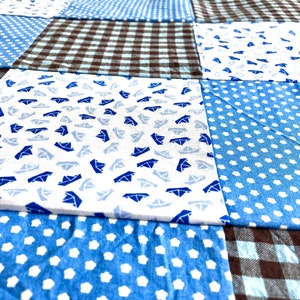 Puede incluir: Una colcha de retazos con una variedad de telas azules y marrones. La colcha est&aacute; hecha de cuadrados con diferentes patrones, incluyendo lunares, cuadros vichy y un patr&oacute;n de peque&ntilde;os veleros.