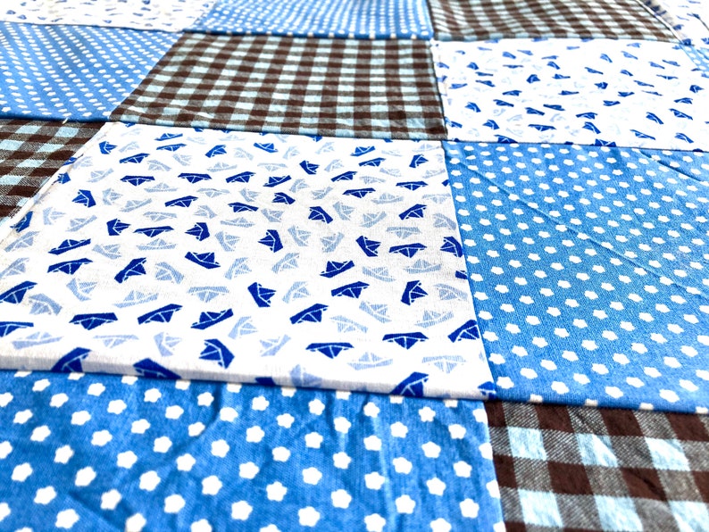Puede incluir: Una colcha de retazos con una variedad de telas azules y marrones. La colcha est&aacute; hecha de cuadrados con diferentes patrones, incluyendo lunares, cuadros vichy y un patr&oacute;n de peque&ntilde;os veleros.