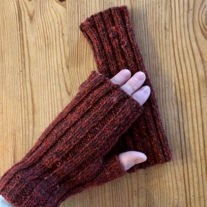 May include: A pair of brown fingerless gloves made of a knitted fabric. The gloves are folded in half and have a ribbed texture.