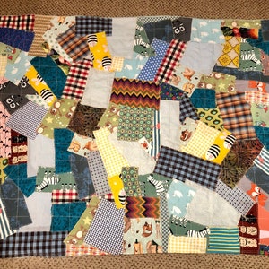 Könnte beinhalten: Eine Patchwork-Decke aus verschiedenen Stoffresten in verschiedenen Farben und Mustern, darunter Blau, Grün, Gelb, Rot und Braun. Die Decke besteht aus Quadraten und Rechtecken aus Stoff, die zusammengenäht wurden, um ein einzigartiges und farbenfrohes Design zu schaffen.