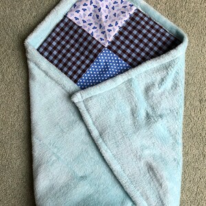 Puede incluir: Una manta de beb&eacute; de felpa azul claro con un dise&ntilde;o de patchwork. El patchwork est&aacute; hecho de cuatro cuadrados de diferentes telas azules y blancas.