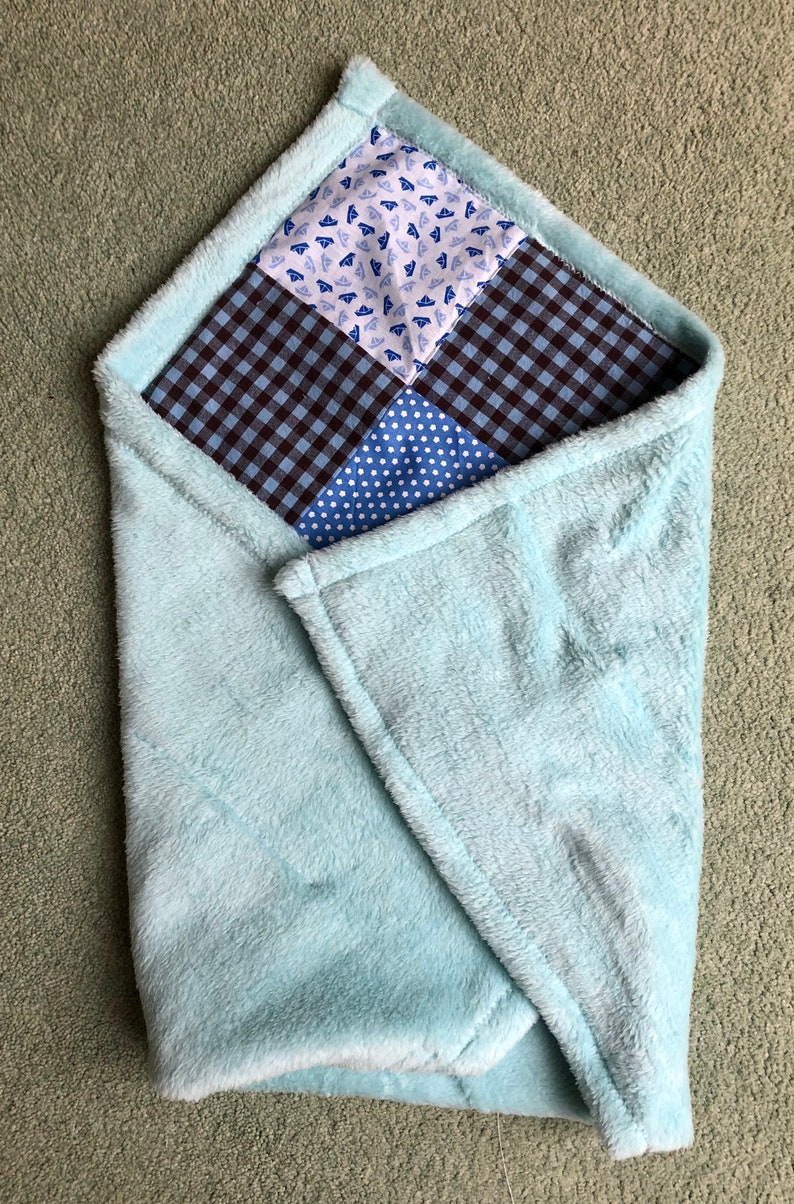 Puede incluir: Una manta de beb&eacute; de felpa azul claro con un dise&ntilde;o de patchwork. El patchwork est&aacute; hecho de cuatro cuadrados de diferentes telas azules y blancas.