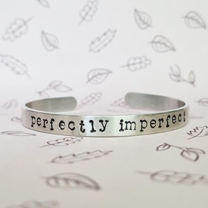 May include: A silver bracelet with the words "perfectly imperfect" engraved on it.
