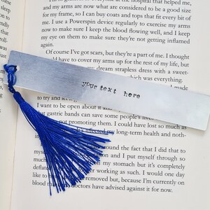 May include: A silver bookmark with a blue tassel. The bookmark is rectangular and has the text "your text here" engraved on it.